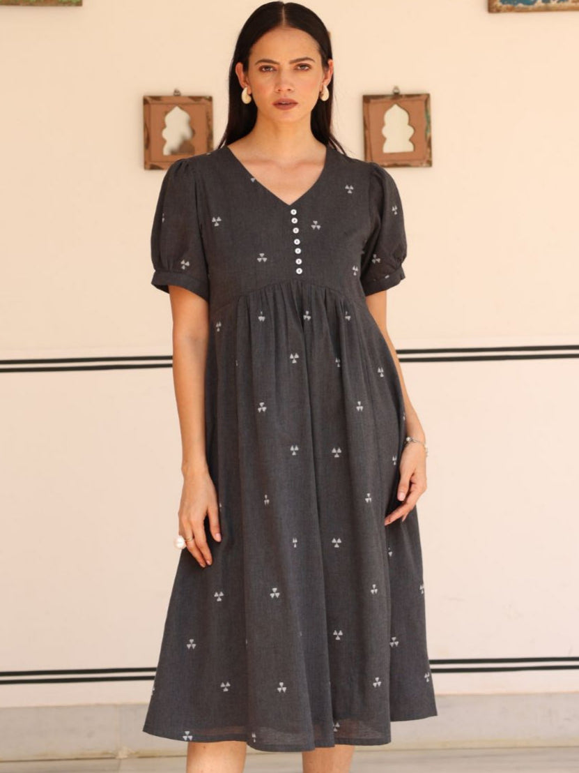 Woman wearing a dark gray dress with white floral patterns against a neutral background